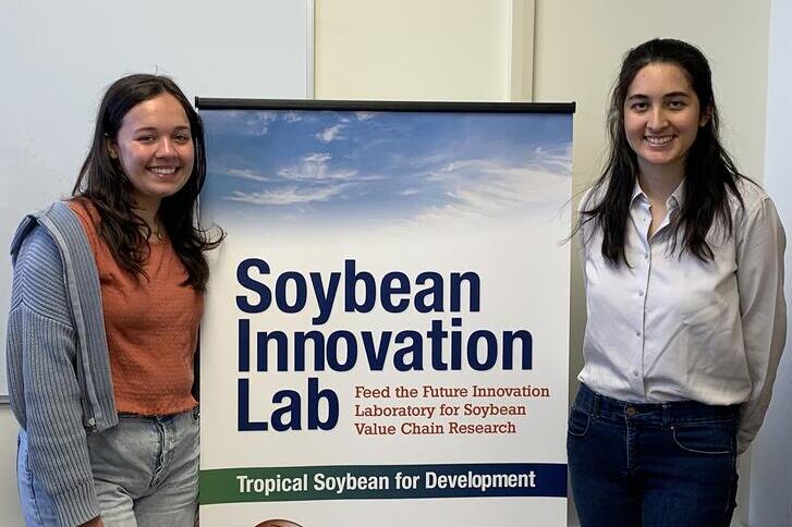 Two women standing on either side of a “soybean innovation lab’ banner in an office setting.  